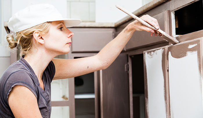 Woman painting kitchen cabinets with a brush for a DIY renovation project