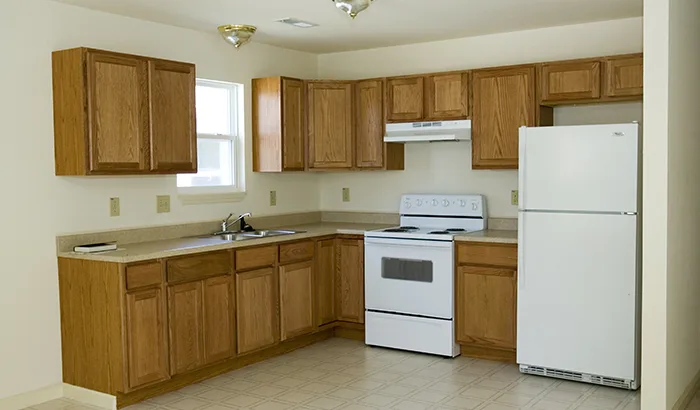 Empty kitchen with old wooden cabinets and white appliances.