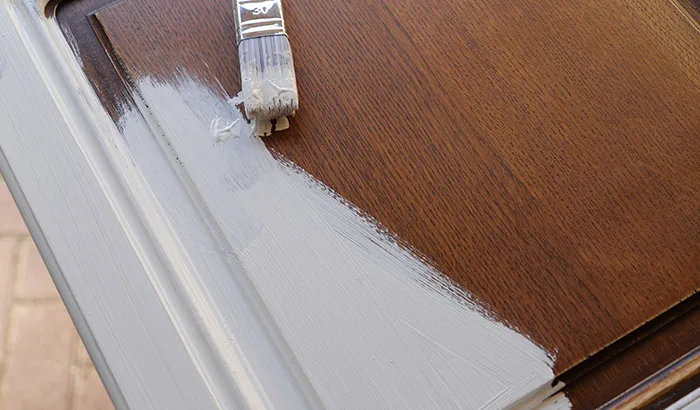 Close-up of a paintbrush applying white paint on a wooden surface.