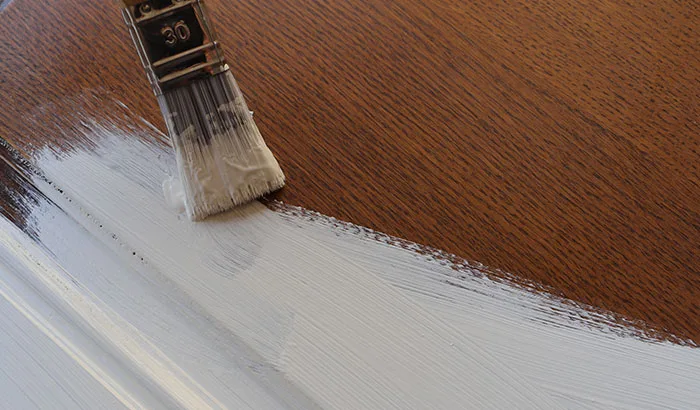 Close-up of a paintbrush applying white paint on a wooden surface.