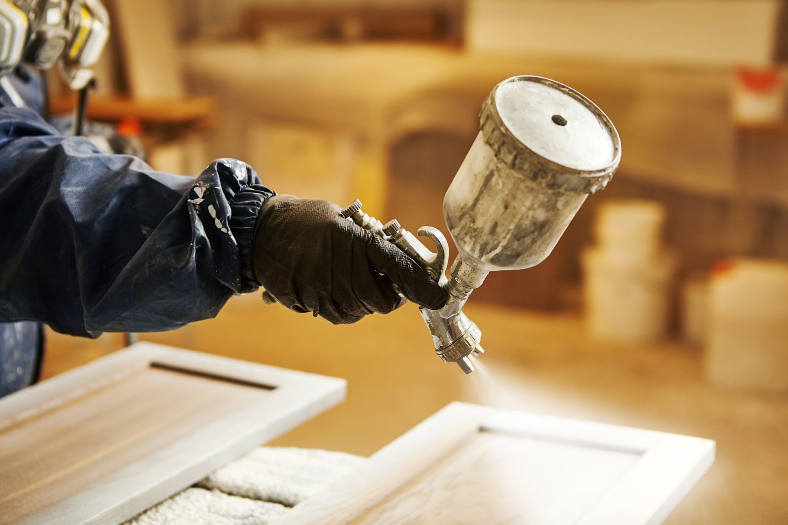 A person in a blue jacket applies paint to a wooden cabinet, showcasing a cabinet painting service in action.