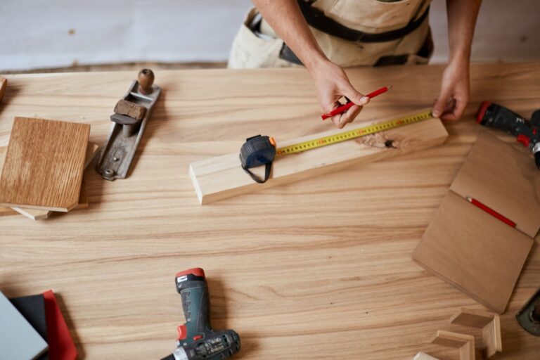 A man diligently works on a wooden table, surrounded by tools, focusing on cabinet painting and kitchen renovations.