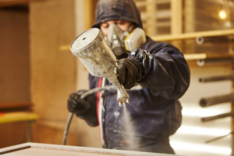 Individual in protective gear painting wood with spray gun