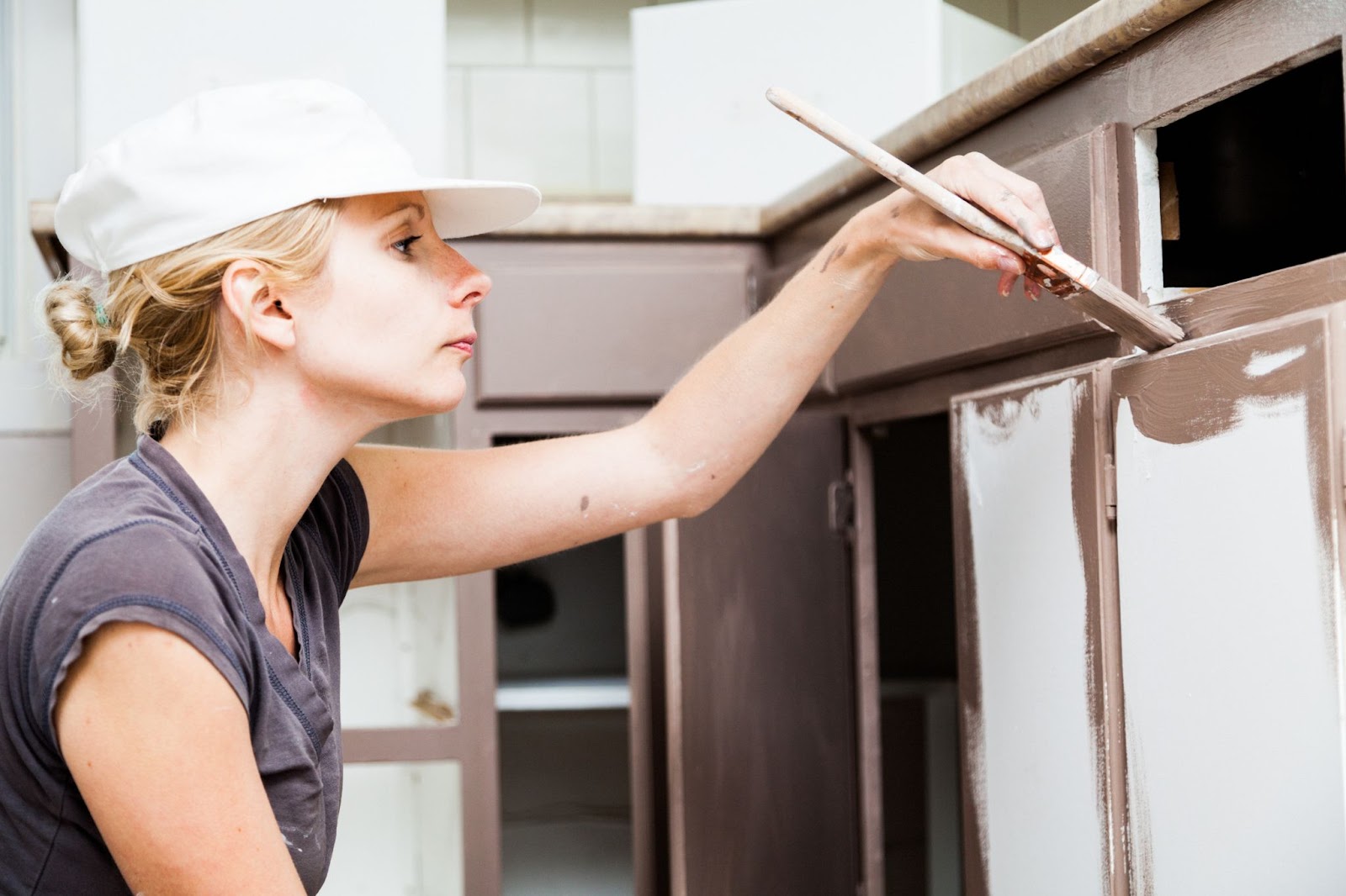 A woman carefully painting a kitchen cabinet, preparing it for a fresh and vibrant finish.