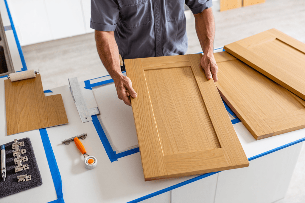 Installer aligning new kitchen cabinet door; wood veneer on face frames, hinges laid out on a padded mat.