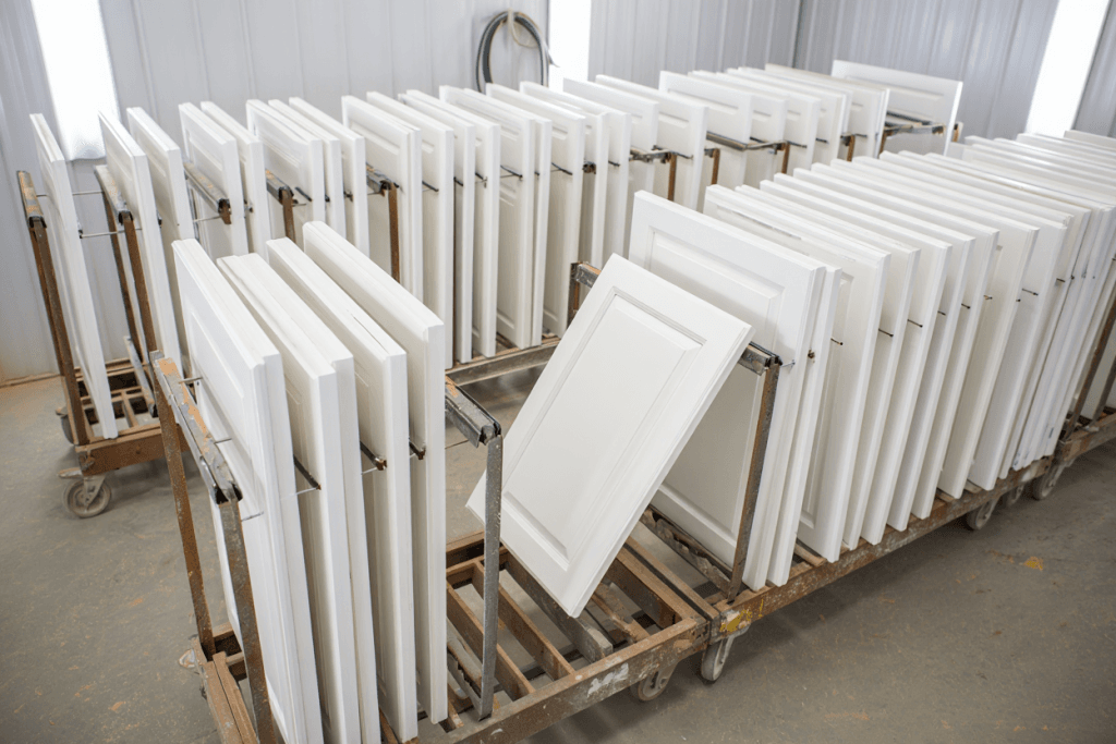 How Much Does it Cost to Paint Kitchen Cabinets in Utah? 2 Stack of white shaker cabinet doors organized on drying racks in a professional spray shop.