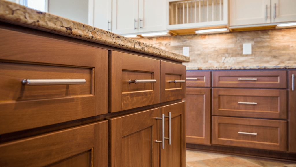 Two-tone kitchen with warm brown-plum lower cabinets, white uppers, and warm stone countertops.