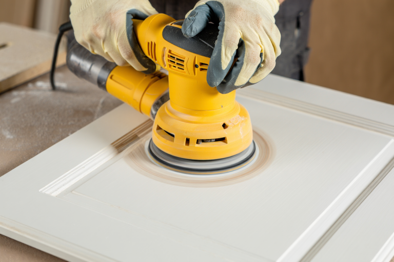 Orbital power sander creating smooth surface on cabinet door during professional kitchen cabinet refinishing preparation in Utah
