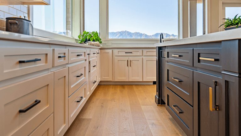 Modern farmhouse kitchen in Utah with white and greige shaker cabinets, wood floors, and large windows showing bright natural light.