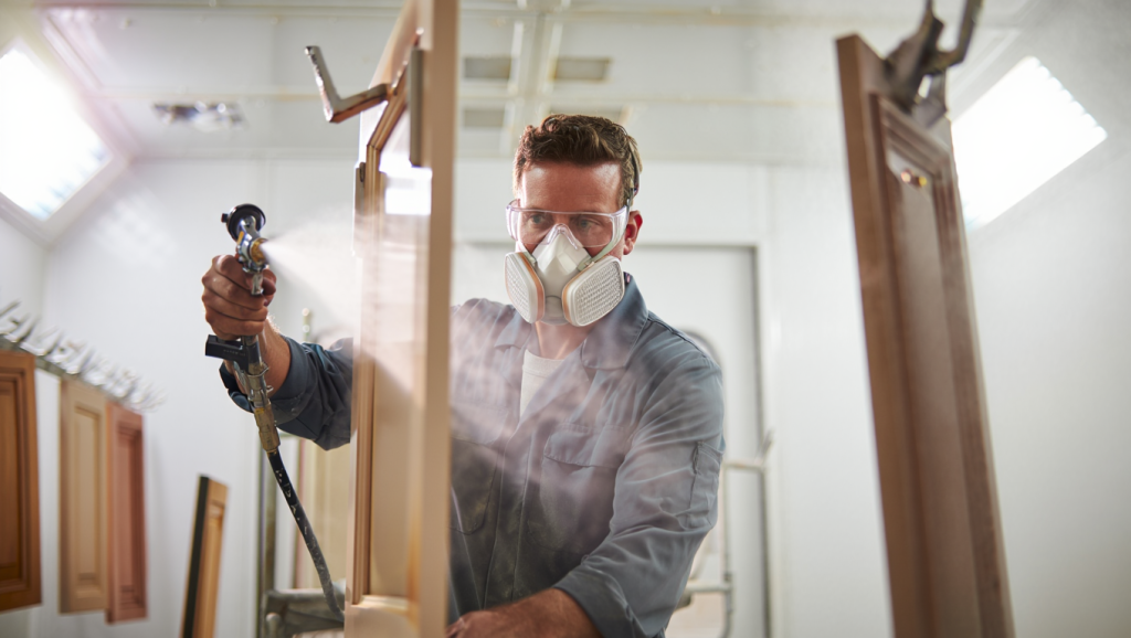 Professional cabinet refinisher using spray equipment on kitchen cabinet doors in workshop