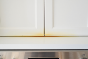 Close-up of white cabinets turning yellow. Painted kitchen cabinet doors near a gas range, showing subtle warm discoloration along the top edge and near the handle