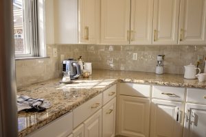 Cabinet paint colors that go with granite shown in a Utah kitchen with warm white satin cabinets above tan and gold granite countertops