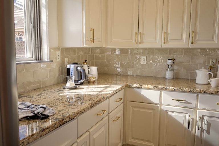 Cabinet paint colors that go with granite shown in a Utah kitchen with warm white satin cabinets above tan and gold granite countertops